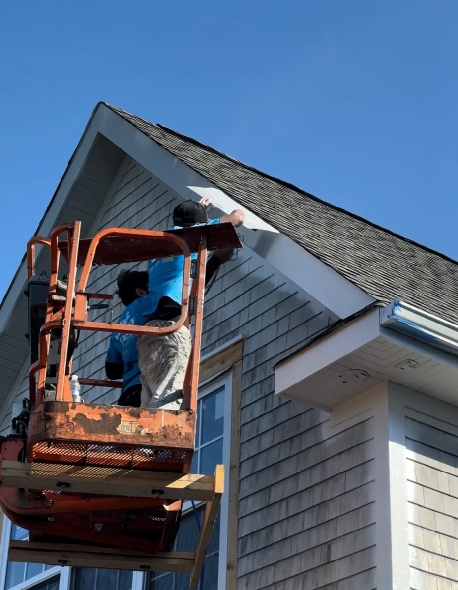 Brush Buds crew painting a house exterior from a lift